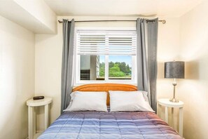 A bedroom with a bed, a window with curtains, a bedside table, and a lamp. - 1BR Condo | Dogs OK | Close to Ocean & Town (Ocean Shores)