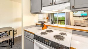 A compact kitchen with a stove, cabinets, and a dining table. - 1BR Condo | Dogs OK | Close to Ocean & Town (Ocean Shores)