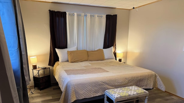 A neatly arranged bedroom with a bed, bedside lamps, a small table, and a bench.