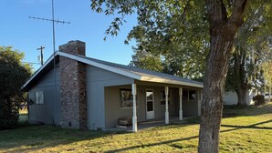 A single-story house with a brick chimney, a porch with white columns, and a clear sky.