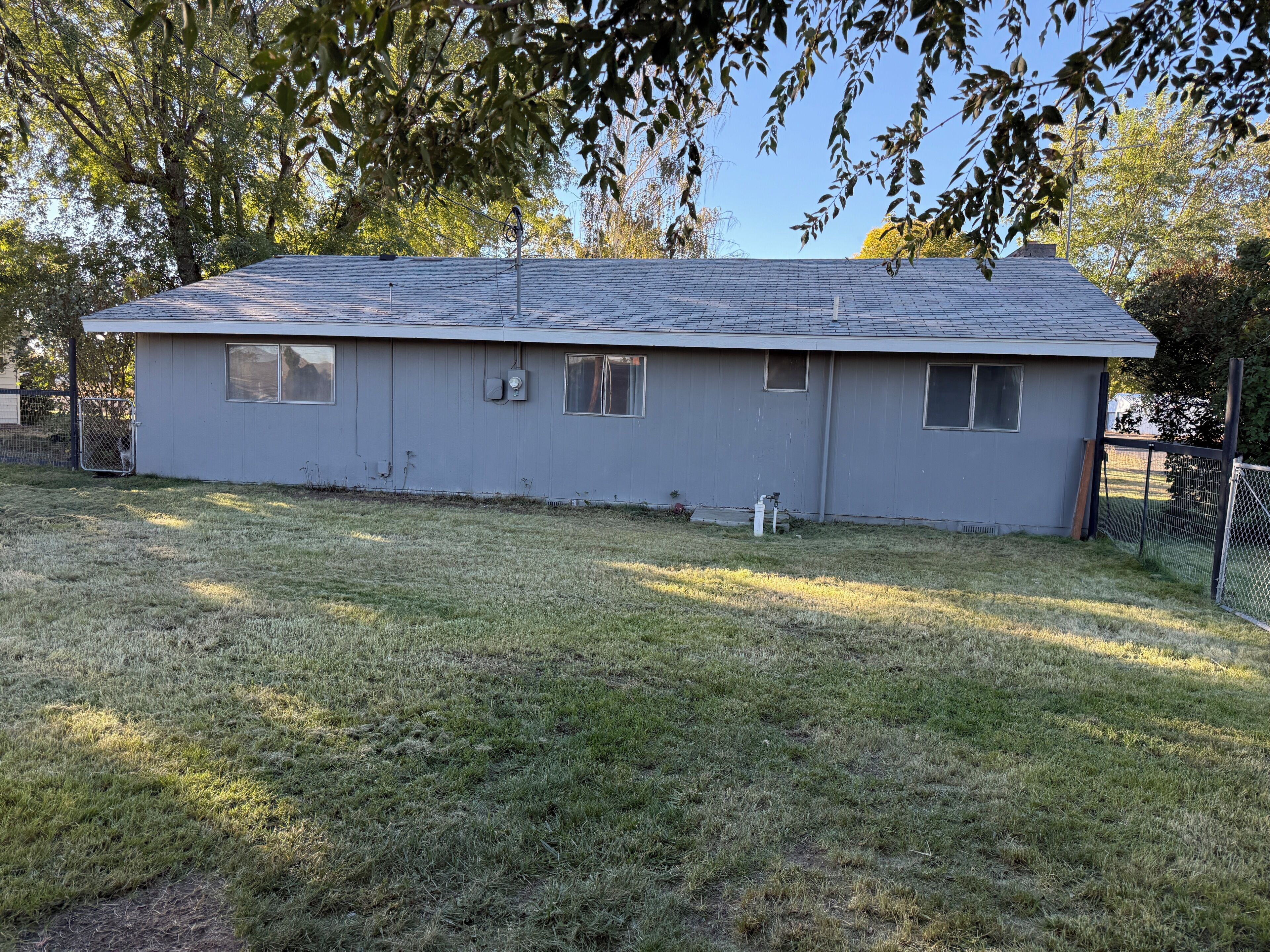 A single-story building with a flat roof, a fenced yard, and a small tree in the background.