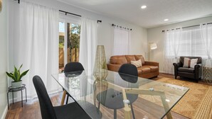 Uma sala de estar com uma mesa de jantar de vidro, duas cadeiras pretas, um sofá de couro marrom e uma poltrona preta.
