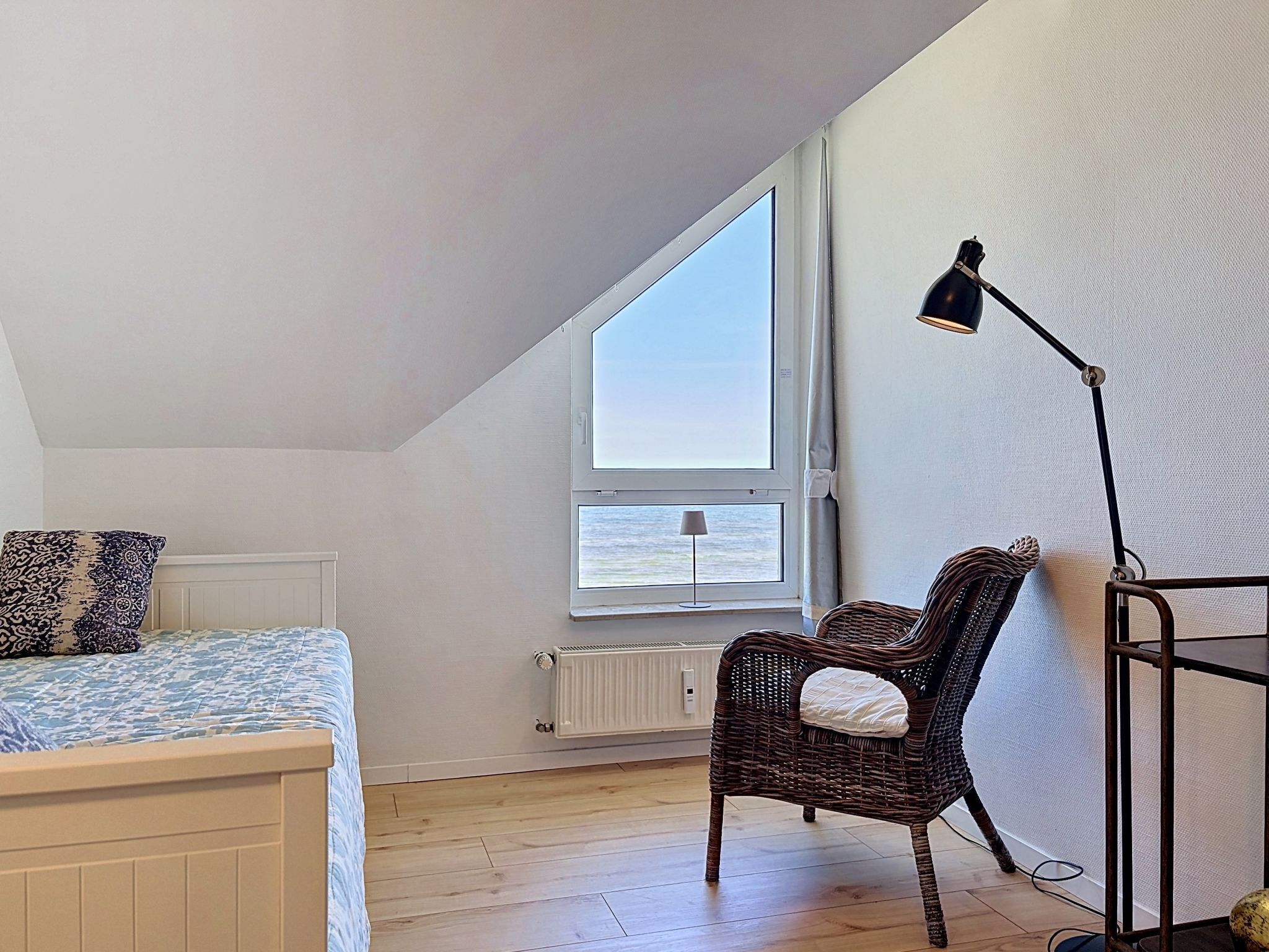 A bedroom with a large window, a bed, a chair, and a floor lamp.
