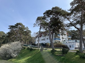 Ein großes, mehrgeschossiges Gebäude mit weißer Fassade und blauen Akzenten, umgeben von üppiger Vegetation und Bäumen.