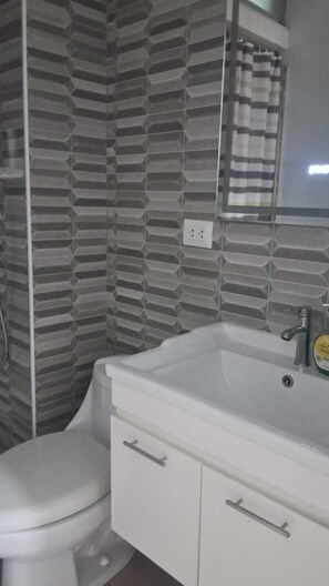 Une salle de bain avec des toilettes, un lavabo avec un miroir et un mur décoré d’un motif.