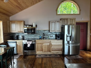 A kitchen with wooden cabinets, a stainless steel refrigerator, a microwave, and an oven. - Beautiful 1 bedroom Treehouse  with heart shaped hot tub (Bee Branch)