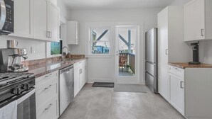 Een moderne keuken met witte kastjes, een inbouwoven, een koffieapparaat en uitzicht door een glazen deur op een terras.