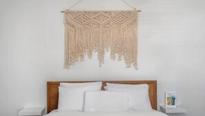 Een bed met witte beddengoed, een houten hoofdbord en een macramé wanddecoratie.