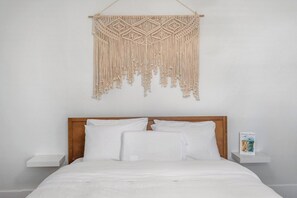 Een bed met witte beddengoed, een houten hoofdbord en een macramé wanddecoratie.