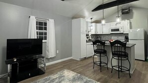 Een moderne keuken met witte kasten, een eethoek met twee barkrukken, een flatscreen-tv en een plafond met zichtbare balken.