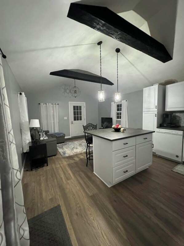 A modern kitchen with a central island, pendant lights, and a dining area with a sofa and table. - Cozy Tiny Home Unit C (Salem)