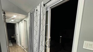 Een gang die leidt naar een balkon met een schuifdeur van glas, een houten vloer en een grijze vloerkleed.