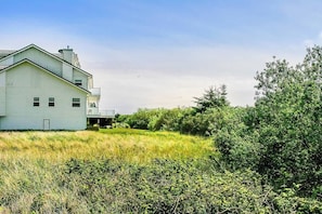 A white building with a gabled roof, surrounded by dense greenery and a clear sky.
