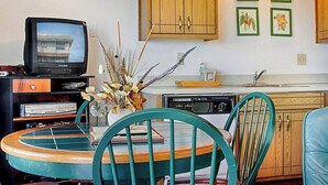 Een keuken met houten kastjes, een eettafel met stoelen, een televisie en ingelijste foto's aan de muur.