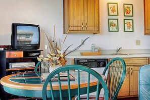 A kitchen with wooden cabinets, a dining table with chairs, a television, and framed pictures on the wall.