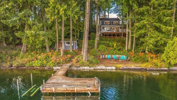 A lakeside cabin with a dock extending into the water, surrounded by dense forest. - Lakefront House: Private Dock, Forest Views, (Shelton)