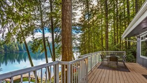 A wooden deck with a railing, overlooking a lake and surrounded by trees. - Lakefront House: Private Dock, Forest Views, (Shelton)