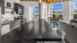 A modern kitchen with a long island, stainless steel appliances, and a view to an outdoor seating area. - Bremerton Bay Condo | Walk to Ferry | Unit 201 (Bremerton)