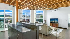 A modern kitchen with a large island, wooden ceiling beams, large windows, and a cityscape view. - Bremerton Bay Condo | Walk to Ferry | Unit 201 (Bremerton)