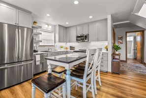 A modern kitchen with stainless steel appliances, a central island, and a dining area with white chairs.