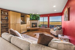 A living room with a fireplace, wooden cabinets, a sofa, and a large window with a view.