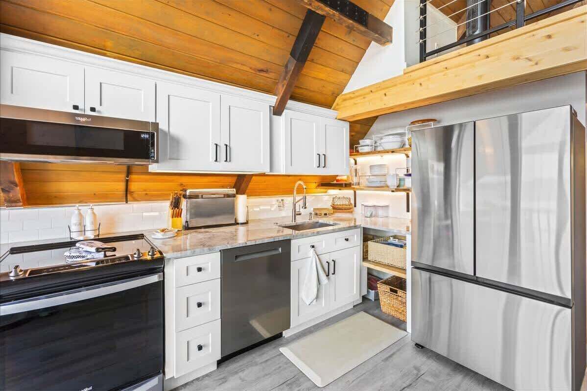 A modern kitchen with white cabinets, stainless steel appliances, and a wooden ceiling.