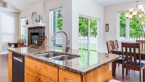 Eine Küche mit Granitarbeitsplatte, Spüle aus Edelstahl, Holzschränken, einem Kamin und einem Essbereich mit Stühlen und Tisch.
