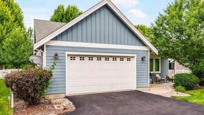 Ein eingeschossiges Haus mit Garage, Satellitenschüssel und einer kleinen Veranda mit Sitzgelegenheit.