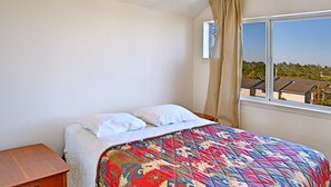 Une chambre à coucher avec un lit, une table de chevet, une fenêtre donnant sur des arbres et des immeubles, et un rideau.