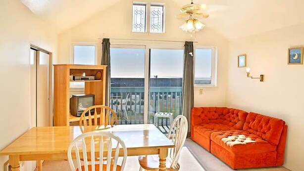Une pièce comprenant une table à manger, des chaises, un canapé, un téléviseur et un balcon avec vue.