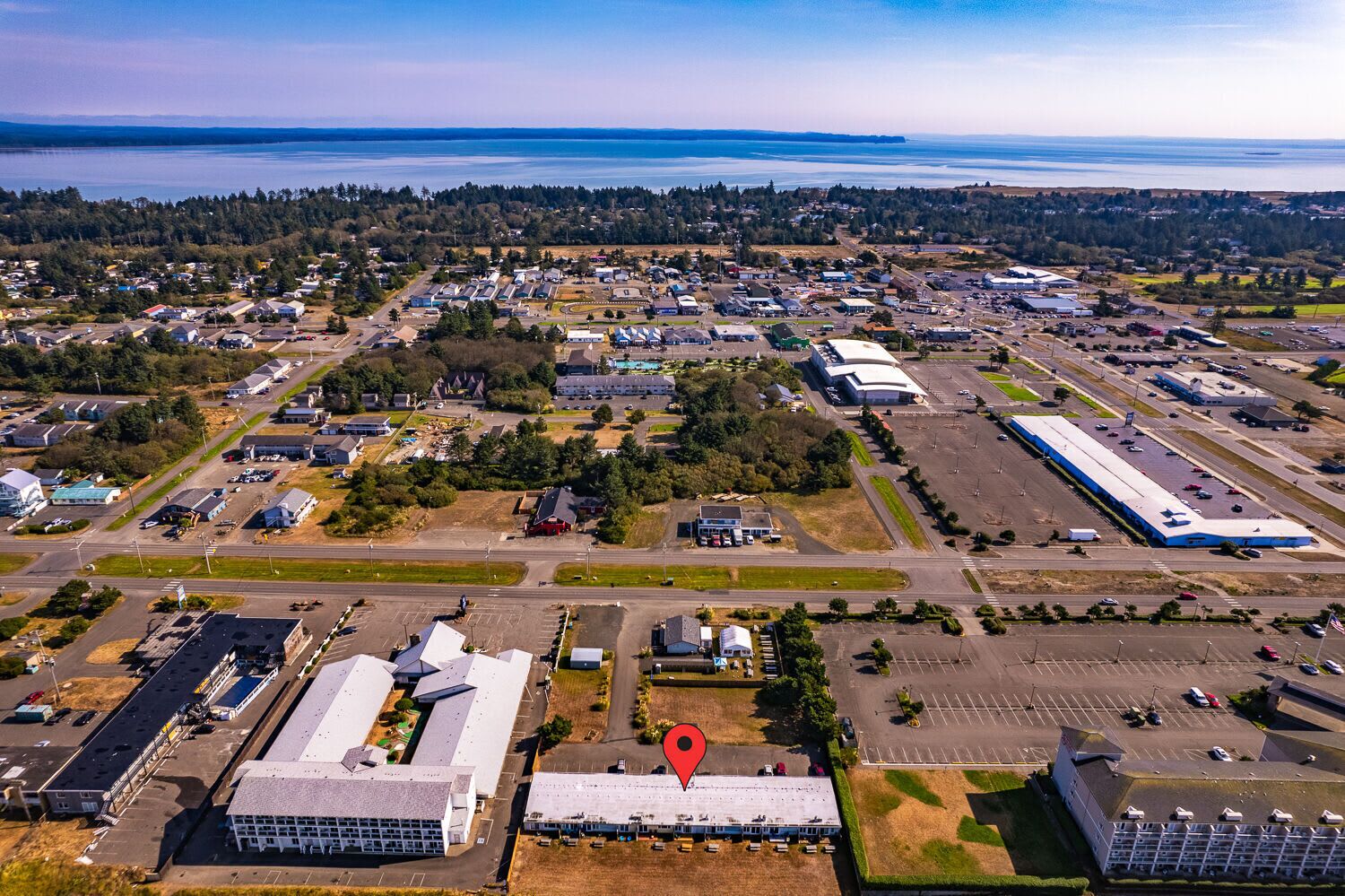 An aerial view of a commercial area with multiple buildings, parking lots, and a large body of water in the background.