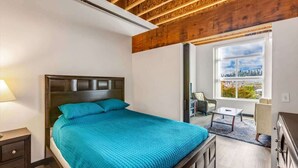 A bedroom with a bed, bedside table, dresser, and a window with a view. - Bremerton Bay Condo | Walk to Ferry | Unit 202 (Bremerton)