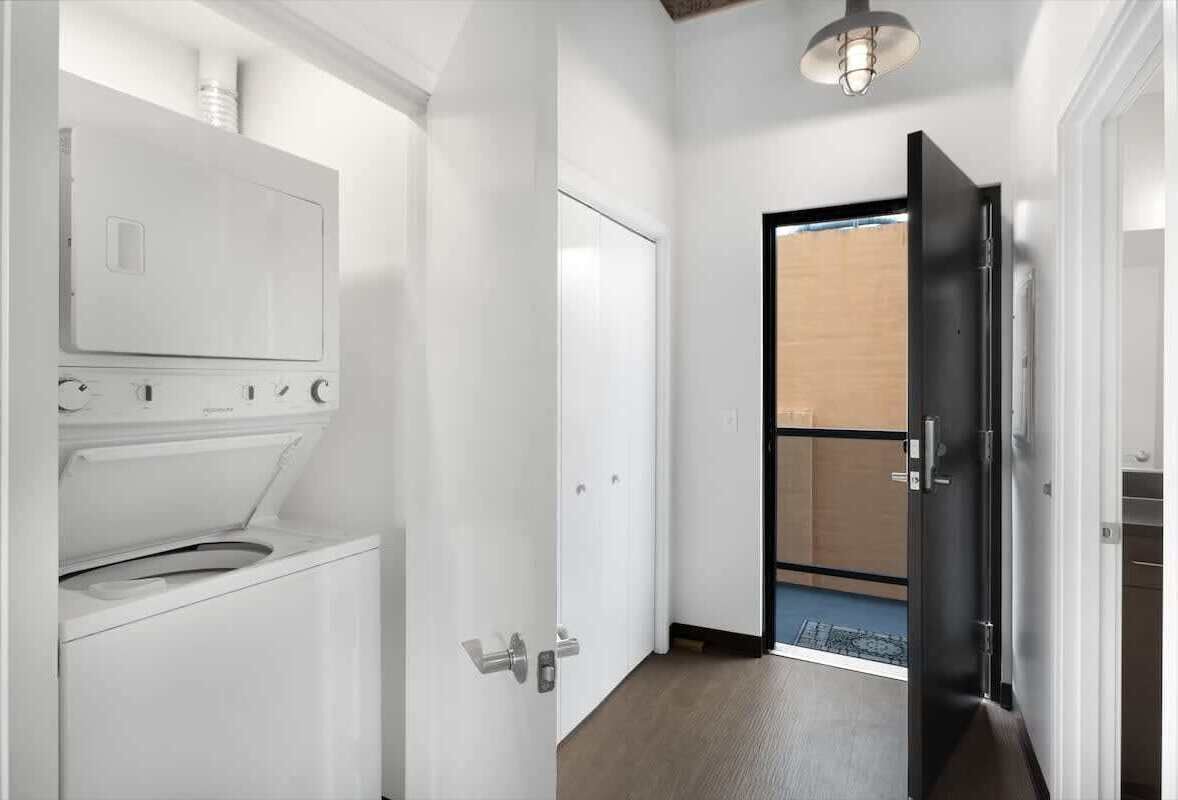 Una lavanderia con lavatrice e asciugatrice, una porta che dà su una stanza con vista e un corridoio con una porta.
