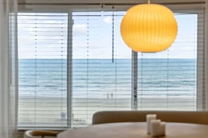 A room with a large window overlooking a beach, a hanging light fixture, and a table with candles. - The Crestwind - 4BR Oceanfront Unit w/ Pool (Sleeps 10) (North Myrtle Beach)