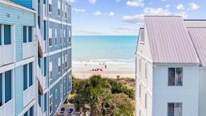A coastal building with a balcony overlooking a beach. - The Sandstone - 4BR Oceanfront Unit w/ Pool (Sleeps 10) (North Myrtle Beach)