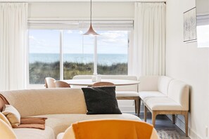 A modern living room with a sofa, a dining table, and a view of the ocean. - The Sandstone - 4BR Oceanfront Unit w/ Pool (Sleeps 10) (North Myrtle Beach)