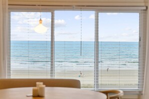 Ein Zimmer mit großem Fenster mit Blick auf einen Strand, einer Hängelampe und einem Tisch mit Kerzen.