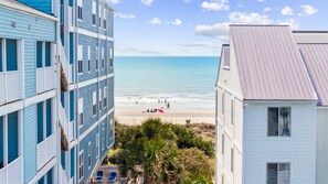 Ein Strandgrundstück mit einem mehrstöckigen Gebäude, einem weißen Haus und Blick auf den Strand.