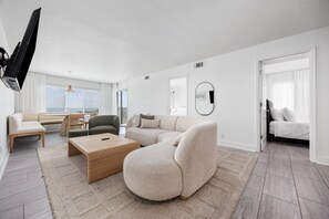 Ein modernes Wohnzimmer mit einer Eckcouch, einem Couchtisch, einem Fernseher und einem großen Fenster.