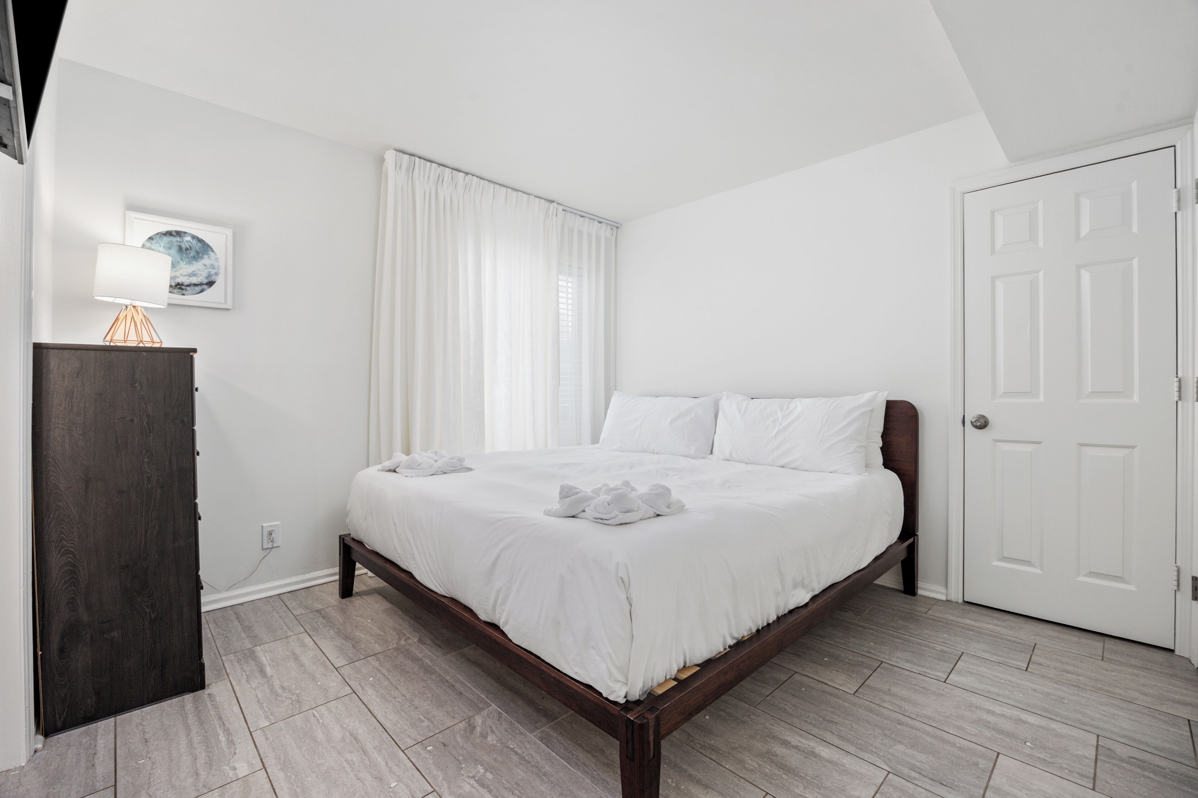 Une chambre à coucher avec un lit, une table de chevet, une lampe, une fenêtre avec des rideaux et une porte.