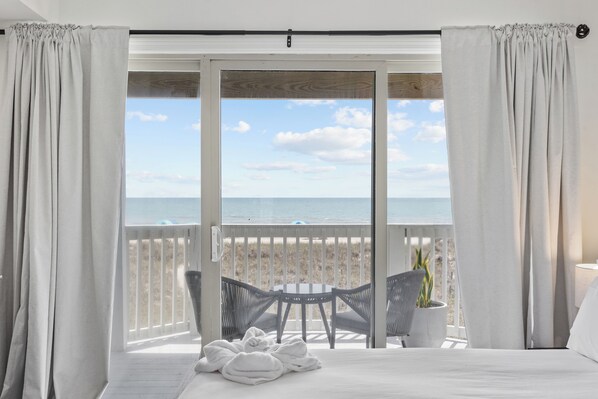 A bedroom with a large window, a bed, a small table, two chairs, and a potted plant. - The Waypoint - 4BR Oceanfront Unit w/ Pool (Sleeps 10) (North Myrtle Beach)