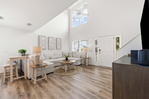 Ein geräumiges Wohnzimmer mit hoher Decke, einem großen Fenster, einer Couch, einem Couchtisch und einem Beistelltisch.