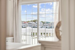 Blick durch ein Fenster mit Gittermuster auf eine Häuserreihe unter blauem Himmel.