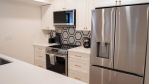 Une cuisine moderne avec des meubles blancs, un réfrigérateur en acier inoxydable, un four à micro-ondes et une cuisinière.