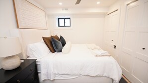 Une chambre à coucher bien rangée, avec un lit, une table de chevet dotée d’une lampe, une commode et une armoire.