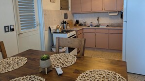A compact kitchen with a gas stove, sink, and a refrigerator. There is a dining table with placemats and a potted plant. - Sun Seekers Retreat-Beaches• Ferry• Cold A/C• Fast WiFi (Santa María)