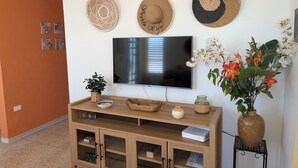 A living room with a flat-screen TV, a wooden cabinet, decorative hats, a potted plant, and a vase with flowers. - Sun Seekers Retreat-Beaches• Ferry• Cold A/C• Fast WiFi (Santa María)