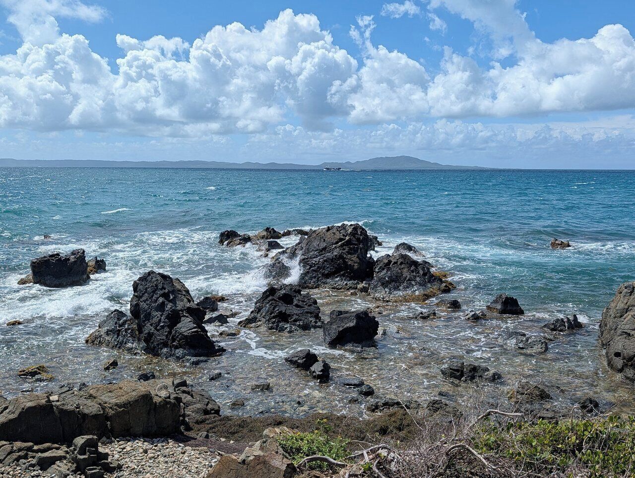 Un littoral rocheux bordé d’une eau d’un bleu limpide et dominé par des montagnes lointaines.