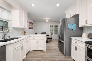Una cocina moderna con armarios blancos, un refrigerador de acero inoxidable y un comedor con mesa y sillas.
