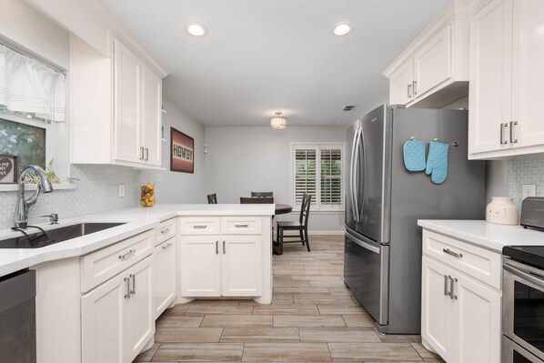 A modern kitchen with white cabinetry, a stainless steel refrigerator, and a dining area with a table and chairs.